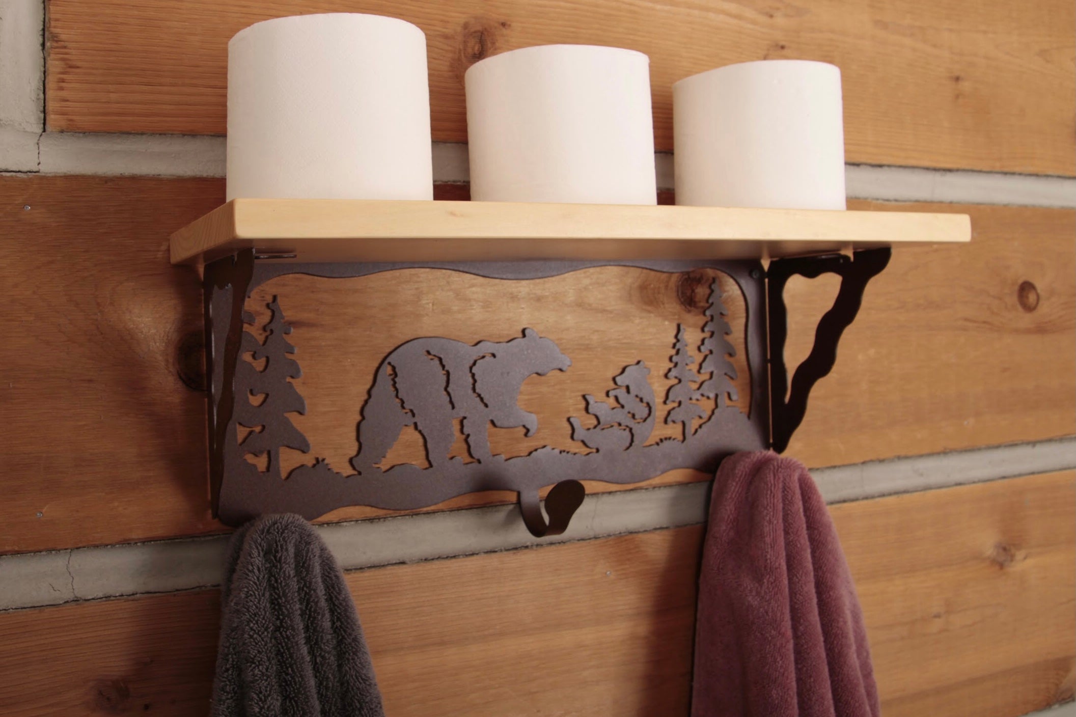 Wooden shelf with bear and tree design, holding toilet paper and towels against a wooden wall.